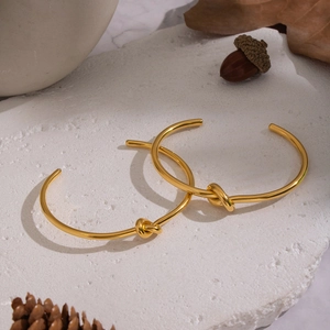Detailansicht von zwei goldenen Edelstahlarmbändern mit Knotendesign auf weißem Naturstein