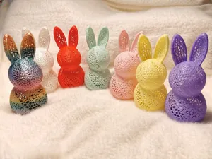 Detail of seven 3D printed hollow rabbit lamps in various colors on white plush background
