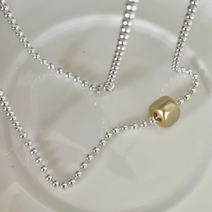 Minimalist 925 silver beaded necklace with a central golden cylinder bead on a white tray