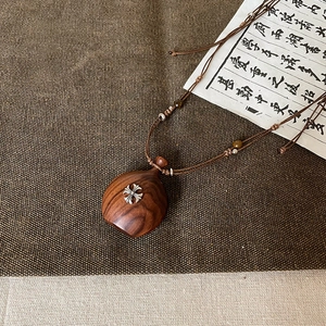 Détail d'un pendentif en bois avec croix métallique et cordon en corde tressée