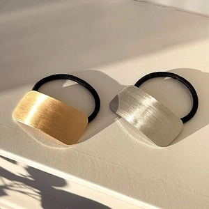 Detail view of gold and silver brushed metal plates on black elastic hair ties