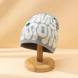 Grey knitted beanie with graffiti-style lettering and green star patterns on a stand