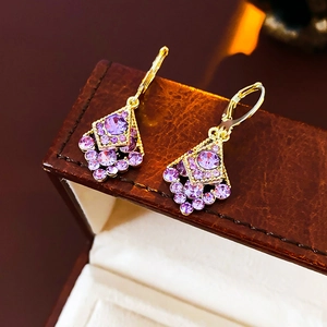 Detailed close-up of gold diamond rhombus earrings with purple gems on leather box