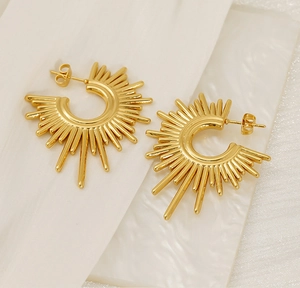 Close-up of golden irregular sunburst geometric earrings on white marble and silk