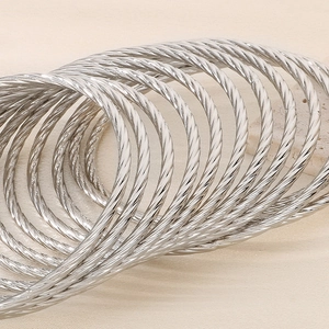 Polished silver stainless steel twisted bangle set with layered spiral texture on beige background