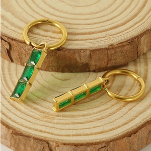 Detail of 18K gold earrings with green zircon pendants on a rustic wood background