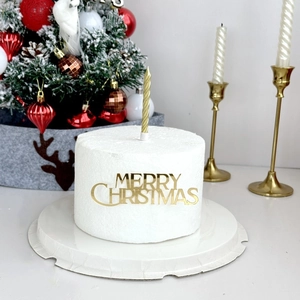 Detail of gold Merry Christmas acrylic cake topper and spiral candle on white cake