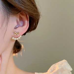 Detailed view of an 18k gold plated bow and pearl ear jacket earring on a model