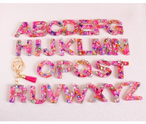 Detail of glitter resin alphabet keychain with pink tassel and colorful stone inlay