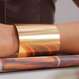Nahaufnahme eines polierten goldfarbenen breiten Armreifs mit minimalistischem Spiegelfinish