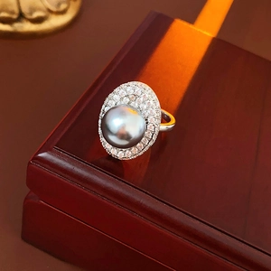Macro shot of an oval grey pearl ring with zircon halo on a dark wooden jewelry box