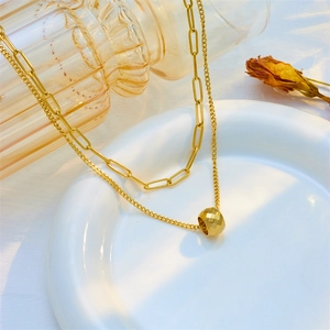 Double-layered gold chain necklace featuring a faceted ball pendant in a ceramic dish