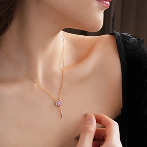 Detail of a gold necklace featuring a key pendant with a pink heart zircon on model