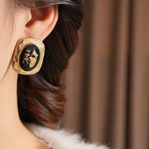 Macro detail of vintage gold oval earring with black enamel and rickshaw relief on model