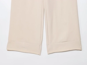 Detail view of beige wide-leg trousers showing cuffed hem and high-quality twill fabric texture