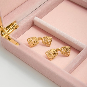 Macro detail of golden hollow lace bow earrings inside a pink velvet jewelry box