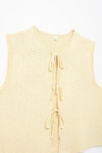 Detail of light yellow knit vest showing hollow crochet texture and three bow tie closures