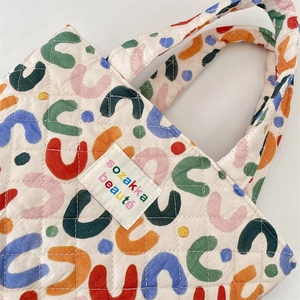 Détail d'un sac cabas matelassé avec motifs en U colorés et étiquette de logo de marque