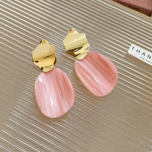 Detail of irregular gold metal earrings with pink marbled oval resin pendants