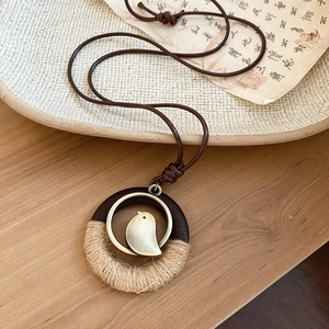 Macro detail of bird charm pendant with wood ring and woven rope on vintage paper