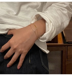 Double-layered gold bracelet with a rectangular pendant worn on a female wrist