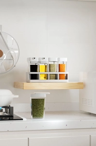 Detail of transparent spice jars with white lids on a matching storage base in the kitchen