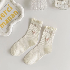 Close-up of white ribbed knit socks featuring delicate pink bows and ruffled edges