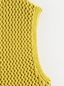 Dettaglio macro del gilet in maglia giallo senape con trama grossa e design traforato