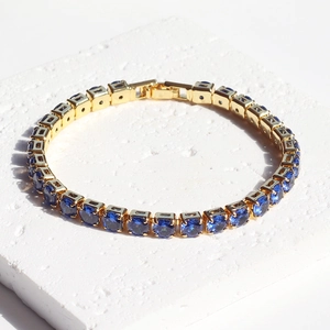 Close-up of golden tennis bracelet with round blue zircons on white stone texture