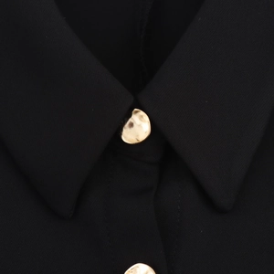 Detail shot of a golden irregular button on textured black sleeveless dress collar