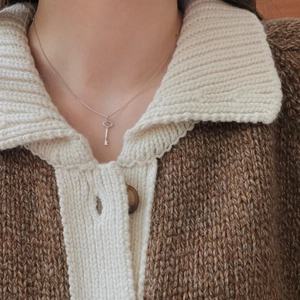 Close-up of minimalist silver key necklace worn by a model over a knit cardigan