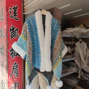 Detail of knit shawl with ethnic zigzag pattern and white faux fur trim and pom-poms