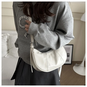 Close-up of a white leather crescent underarm bag worn by a model in a minimalist home setting