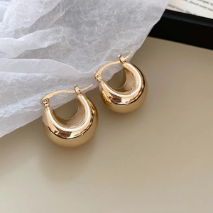 Detail of gold-plated C-shape hoop earrings with a polished metallic finish and clasp design