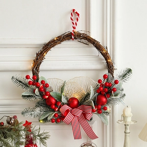 Christmas wreath with red berries, pine cones and warm LED lights on a white wall