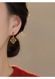 Detail view of hollow flower drop earrings with red gemstone on a model's ear