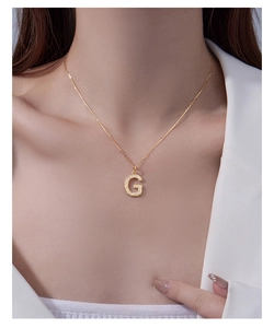 Detailed shot of a gold G-letter pendant necklace set with white cubic zirconia stones