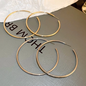 Detailed view of large metallic gold and silver hoop earrings on a textured gift box display