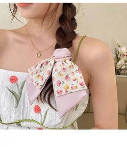 Detail of pink floral bow scrunchie with satin texture styled on a side braid