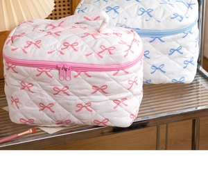 Close-up of quilted cotton cosmetic bag featuring pink bow pattern and zipper detail