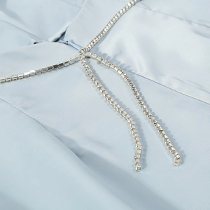 Detail of light blue fabric featuring shimmering silver rhinestone chain tassels on clothing