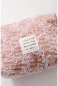 Detail of pink corduroy makeup bag featuring 3D lace flowers and a woven text label