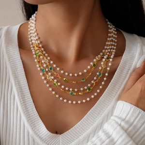 Detail of layered faux pearl and colorful gemstone necklace on model neck with gold chain