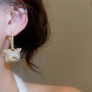 Close-up of golden butterfly earring with a large rectangular zircon pendant on ear