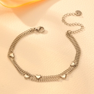 Dettaglio del bracciale argento a doppio strato con cuori su sfondo beige testurizzato