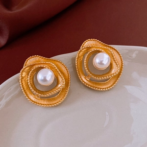 Macro shot of gold hollow flower earrings with white pearl center on velvet tray