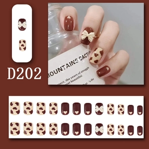 Detail of chocolate brown press-on nails with 3D white bow and cow print patterns