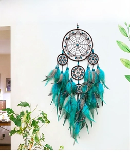 Detail of teal and brown handmade dreamcatcher with feathers hanging on white wall
