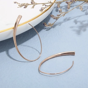 Detail of rose gold teardrop hoop earrings with mirror finish on blue textured background