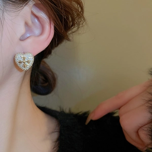 Close-up of heart-shaped gold earring with zircon inlay and cross motif on ear